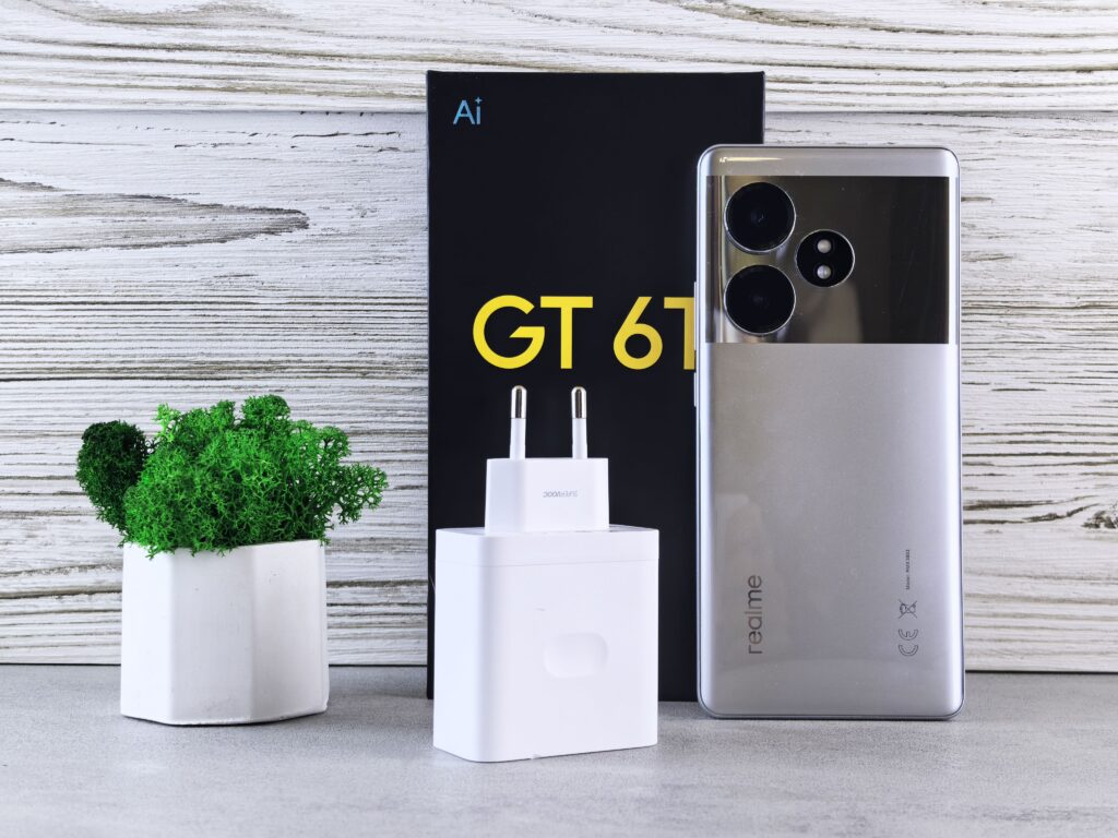 Close-up of a Realme smartphone with charger and potted plant on a wooden surface.